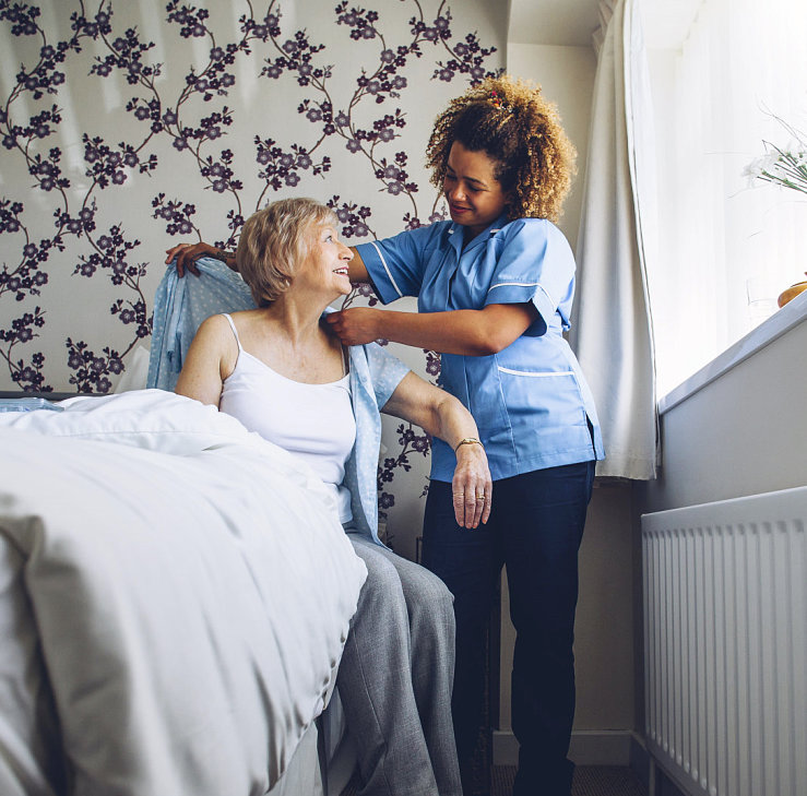 caregiver helping senior woman put on dress